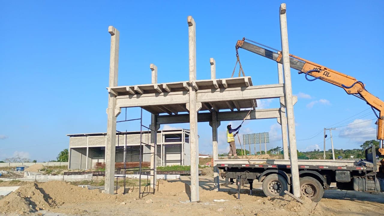 Estrutura pré-moldada com pilares, vigas e peça sendo içada em obra